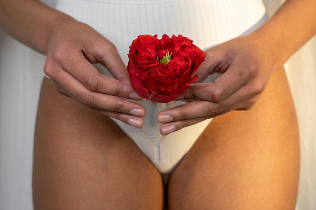 Close-up of hands holding a menstrual cup with a red rose, symbolizing feminine hygiene.