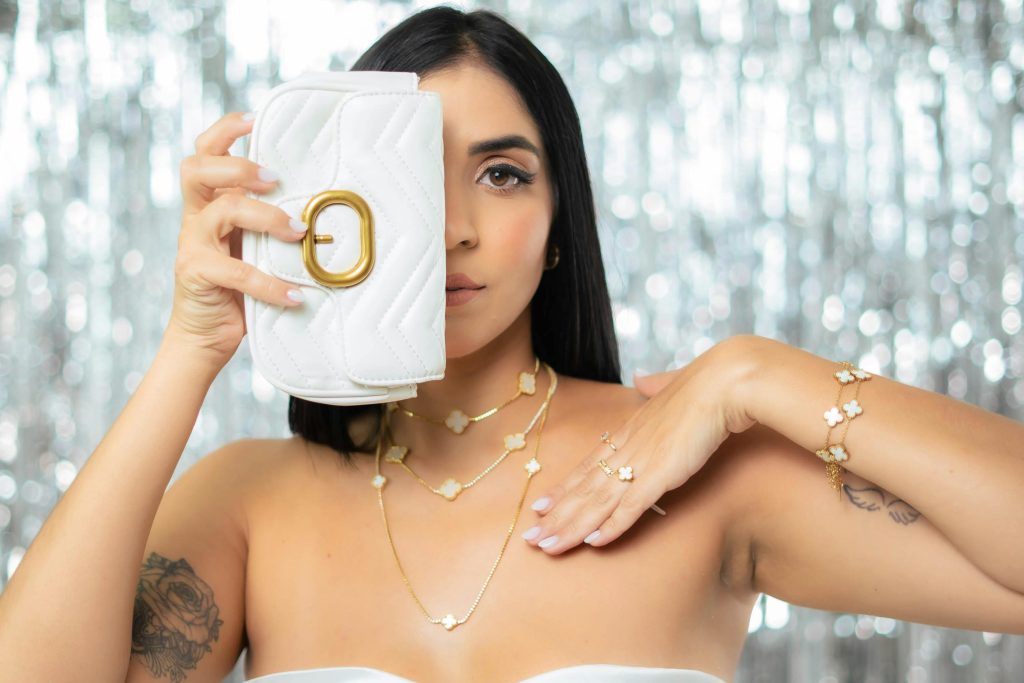Stylish woman showcasing a white clutch and gold jewelry against a sparkling background.