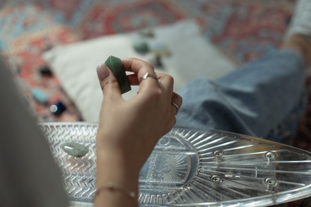Close-up of a hand holding a green gemstone on a patterned glass tray indoors.