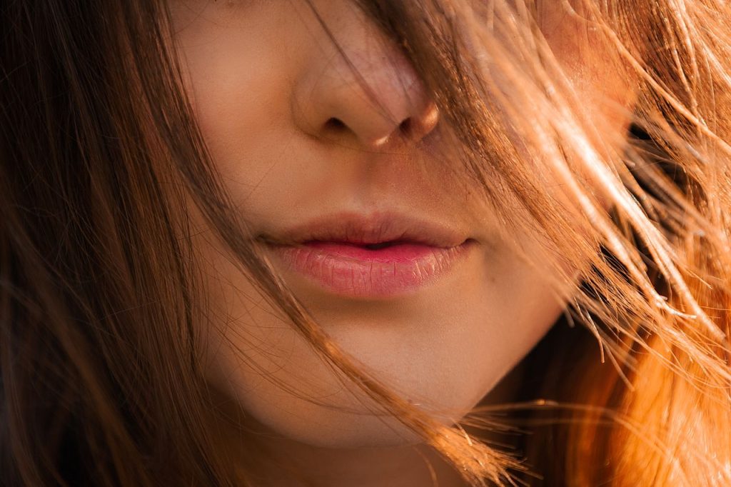 Artistic close-up of a woman's lips partially covered by sunlit hair, showing natural beauty.