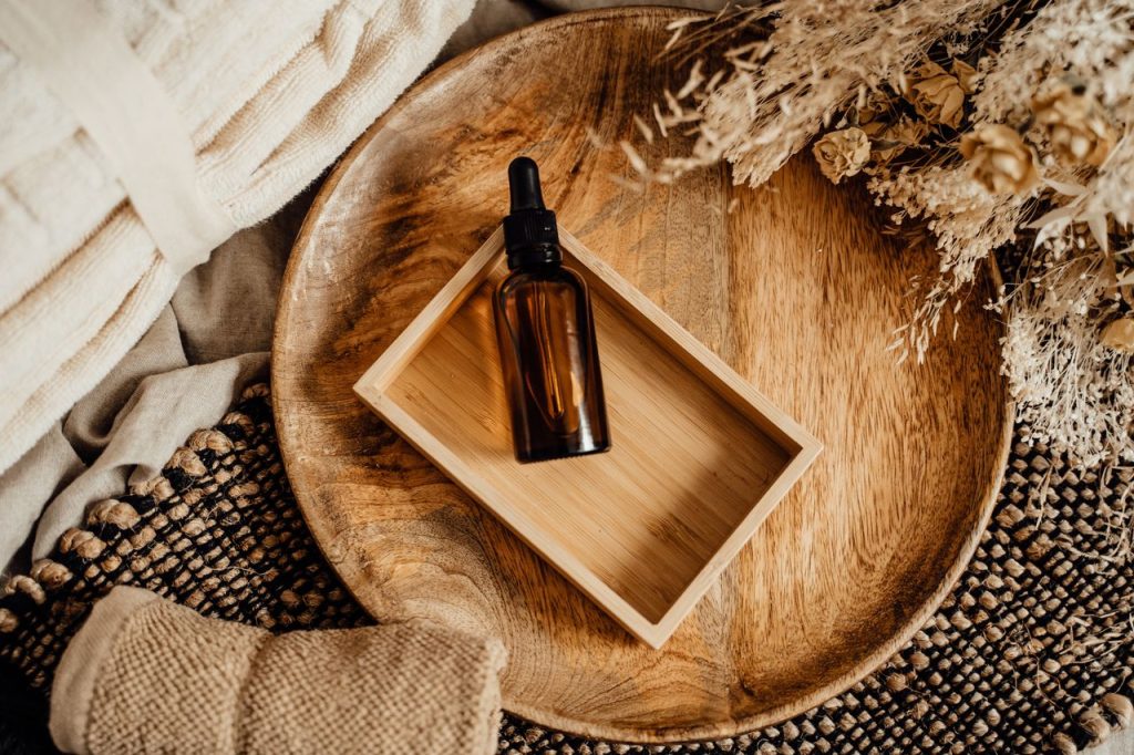 Elegant flat lay of spa essentials with brown glass bottle and wooden tray on rustic fabric.